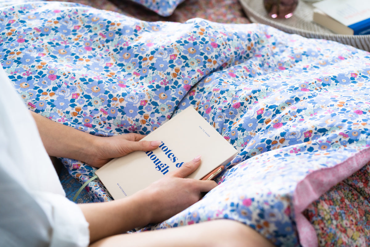 Woman reading in bed, with Liberty fabric bedding including Betsy print
