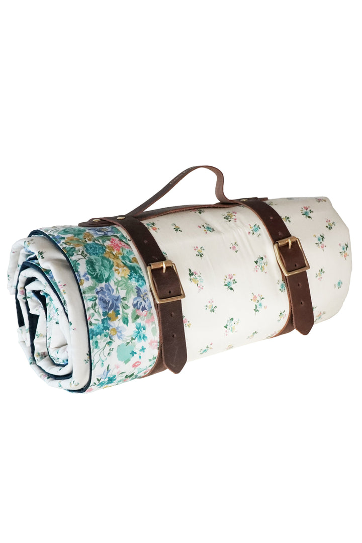 Roll-up floral picnic blanket with brown straps on a white background